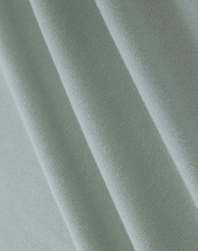 A close-up of light green cotton fabric, featuring a textured weave suitable for polo shirts.