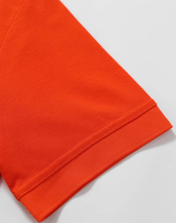 An orange polo shirt featuring a textured fabric and a folded sleeve hem. It includes a logo on the garment.