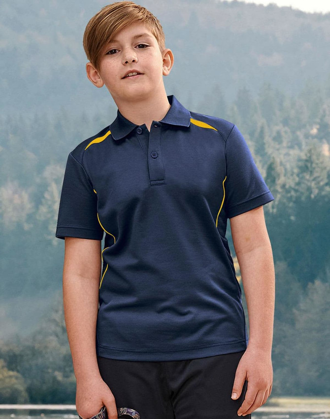 A boy stands outdoors wearing a navy polo shirt with yellow accents and a logo. The background features trees and hills.