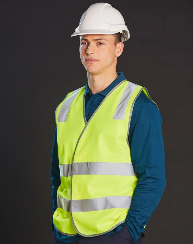 A high visibility safety vest in fluorescent yellow with reflective shoulder tapes, worn over a blue shirt, paired with a white hard hat.