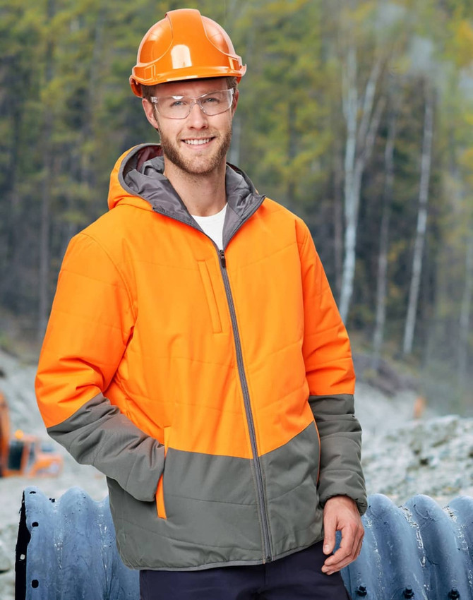 A Hi-Vis quilted two-tone safety jacket in orange and grey, worn by a man in a hard hat and safety glasses, outdoors.