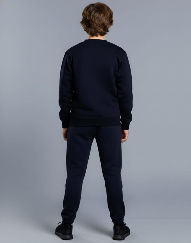 Kid's fleecy trackpants in navy, featuring cuffs, knee padding, and a logo. Worn with a matching navy top.