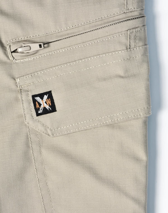 A close-up of light khaki work pants featuring a zippered pocket and a small logo on the side.