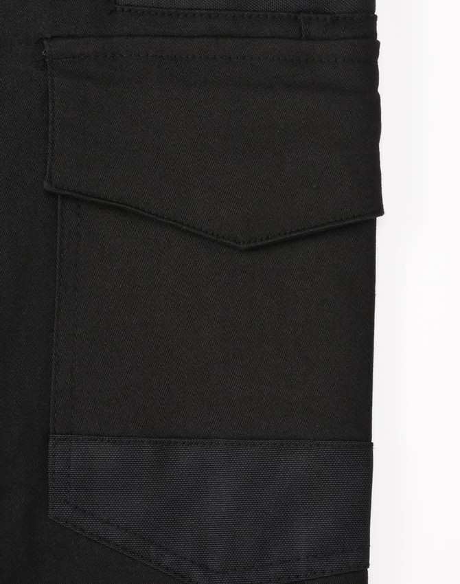 A close-up of black cotton stretch drill cuffed work pants, featuring pockets and a logo.