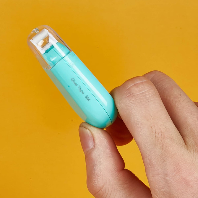 A turquoise glue tape dispenser held in a hand, featuring a clear top and a branding logo.
