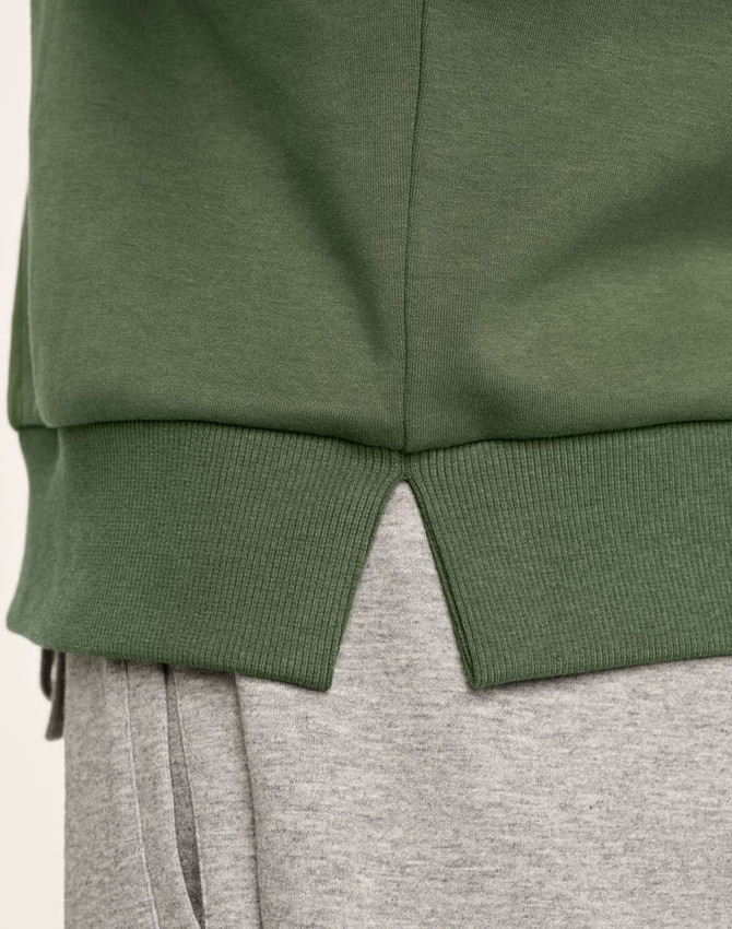 A green crew neck sweater featuring ribbed hem details and a split at the bottom, paired with grey joggers.
