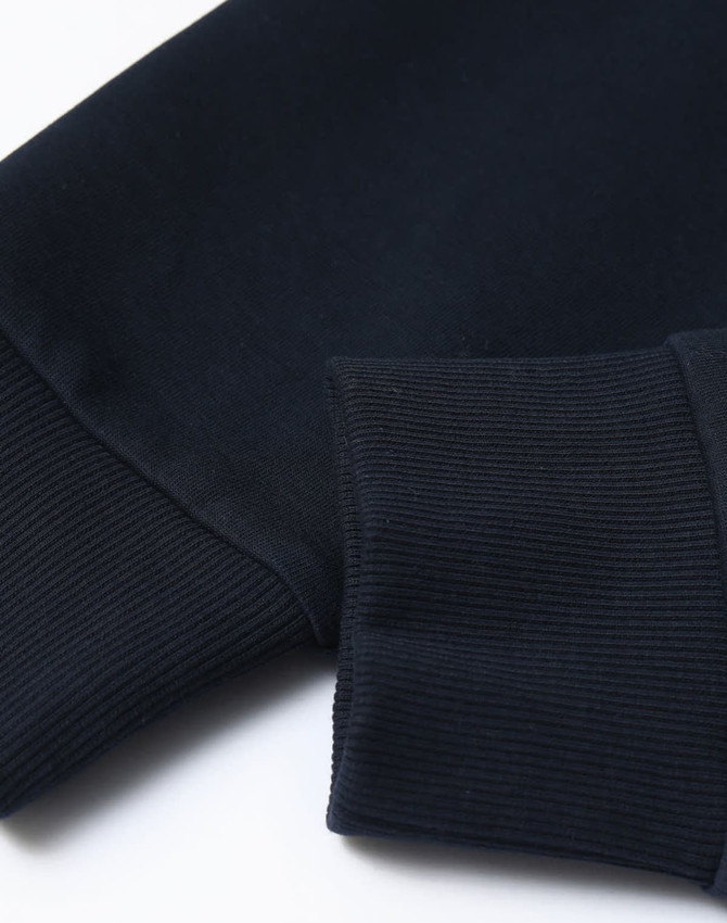 A close-up of a navy unisex crew neck sweater featuring ribbed cuffs and a smooth finish. Contains a logo.