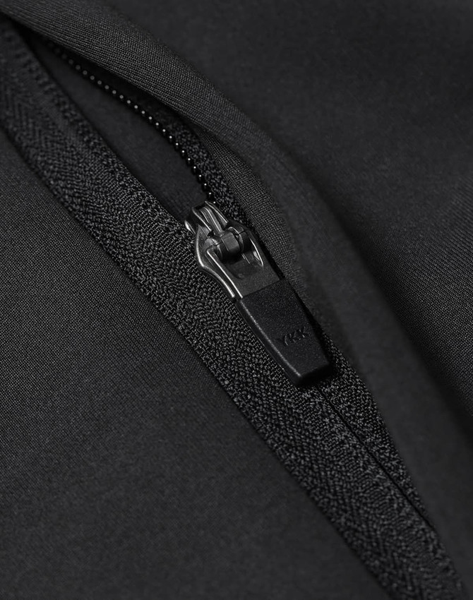 A close-up of a black softshell jacket featuring a zipper detail and a textured fabric finish.