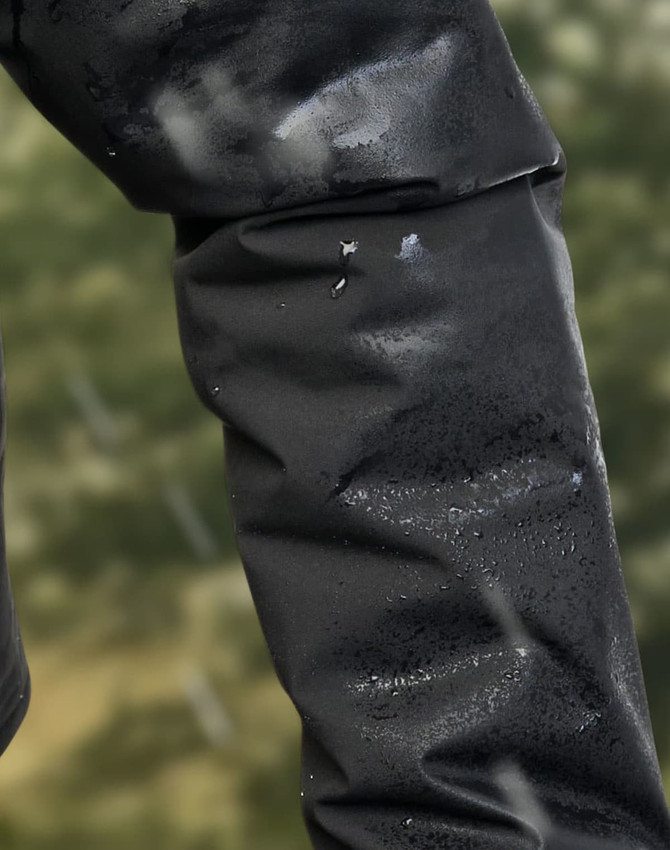 A close-up of a black waterproof jacket sleeve with droplets of water beading on the surface.