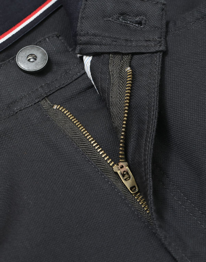 A close-up of a zipper and button detail on black chino pants, featuring sturdy fabric and an internal waistband design.