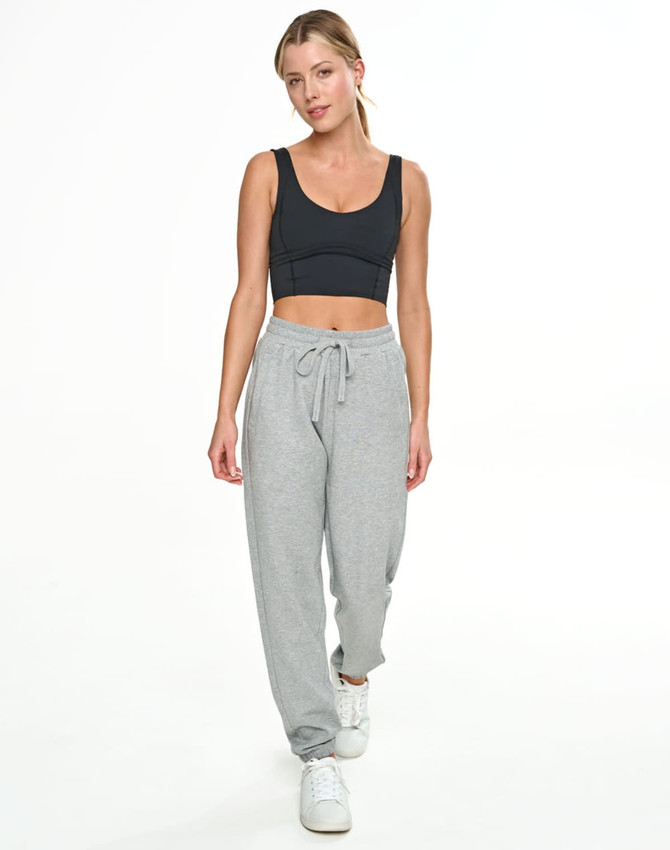 A woman in a black crop top and grey sweatpants stands against a white background. The sweatpants feature a drawstring waist.