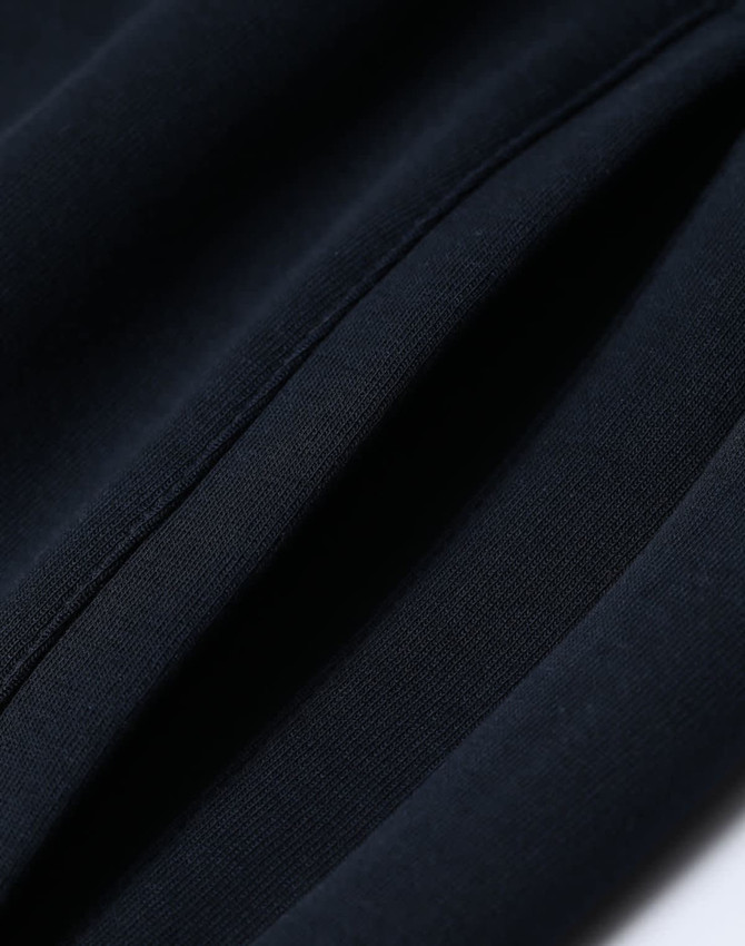 A close-up of navy unisex airlayered CVC sweatpants showing fabric texture and seams. Includes branding.