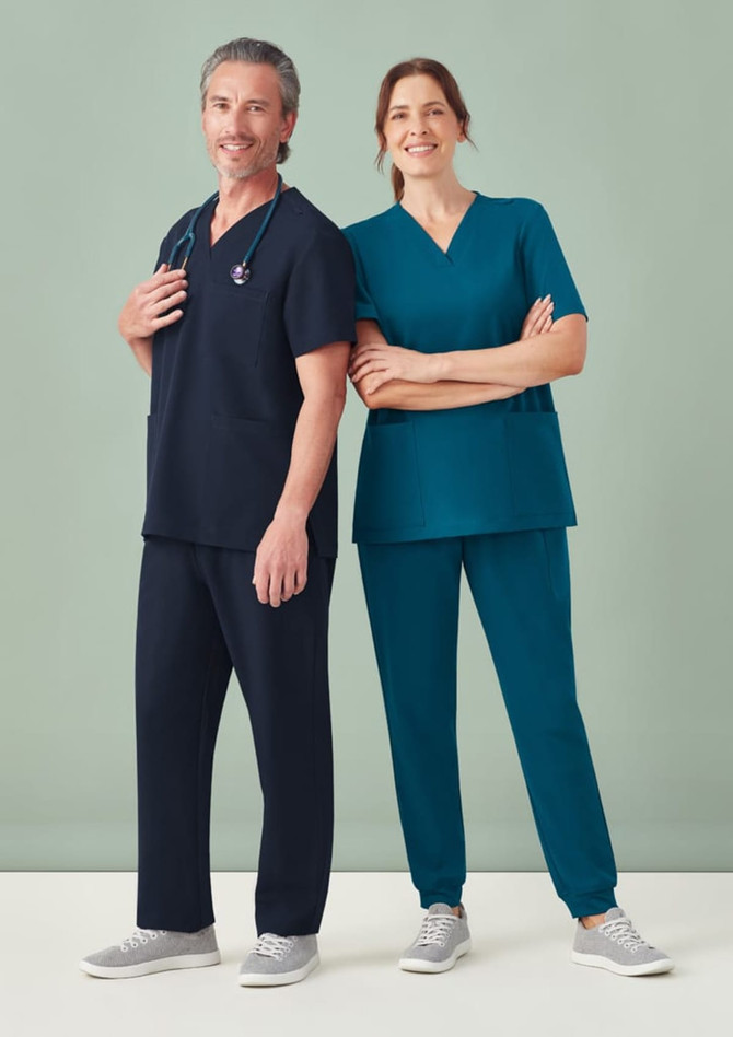 A unisex scrub top in navy and teal, worn by a male and female model, with a stethoscope and casual grey shoes.