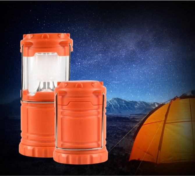 An orange camping lantern set against a starry night sky, with a tent in the background. One lantern is larger than the other.