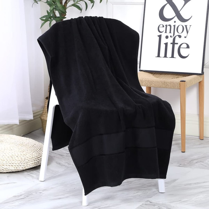 A black bath towel draped over a chair, showcasing its plush fabric and elegant design. There’s a decorative sign in the background.