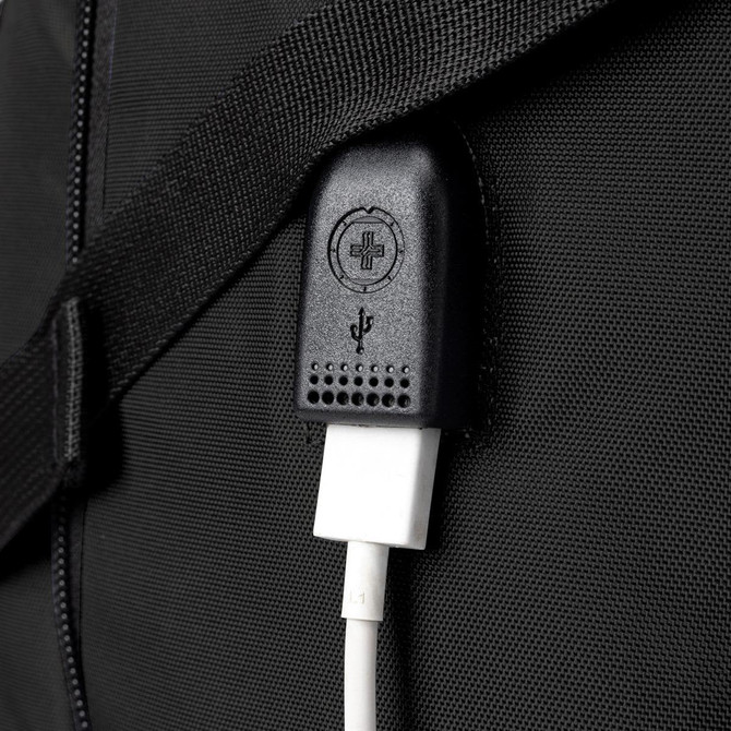 A close-up of a black backpack with a USB charging port and cable attached. It features a textured strap.