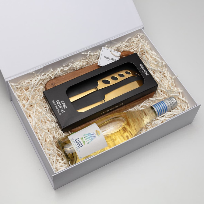 A cheese board set featuring a wooden board, gold knife, and a bottle of white wine in a gift box.