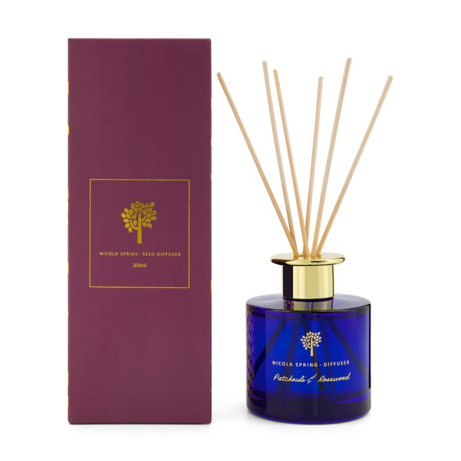 A blue glass reed diffuser with wooden sticks, presented in a purple box. The product is scented with patchouli and aniseed.
