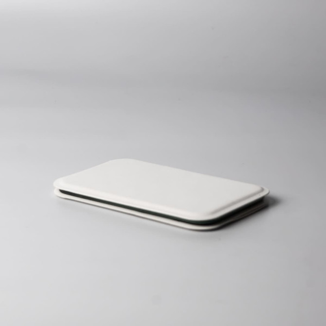 A pocket mirror in sleek white, featuring a minimalist design, resting on a light grey surface.