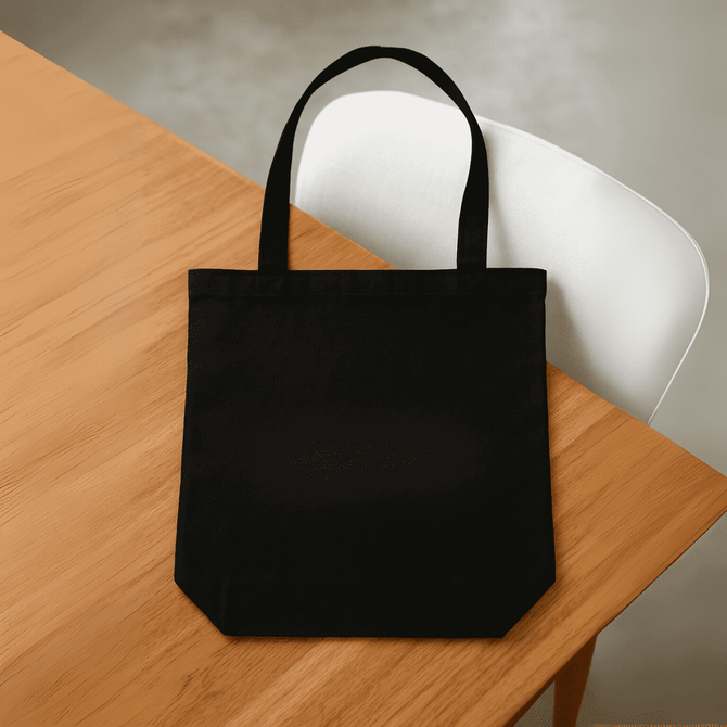 A black tote bag with two handles, placed on a wooden table. The bag has a logo on the front.