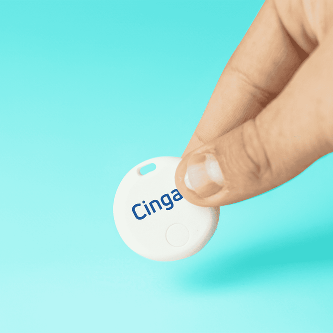 A white circular item tracker held between two fingers, with a blue logo and a smooth surface against a turquoise background.