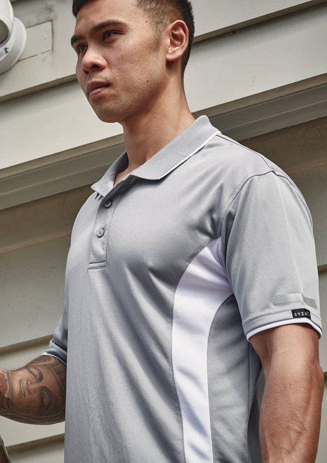 A grey short sleeve polo featuring white accents and a logo on the sleeve. The model is standing outdoors.