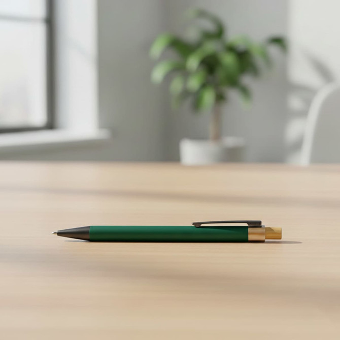 A green metal pen with a gold clip rests on a wooden table, with a plant in the background.