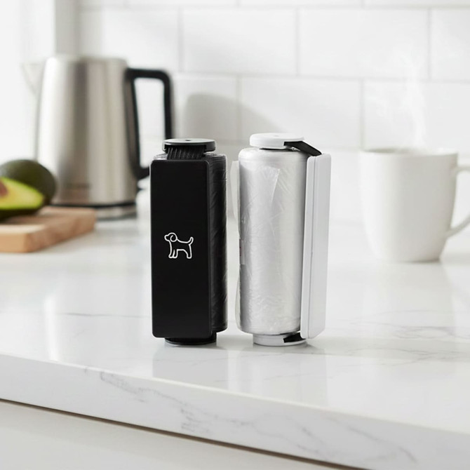 A black and white pet bag dispenser on a marble countertop, featuring a dog logo and neatly held rolls of bags.