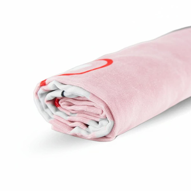 A rolled pink beach towel made of cotton, featuring a subtle pattern and a logo. It measures 80cm x 160cm.