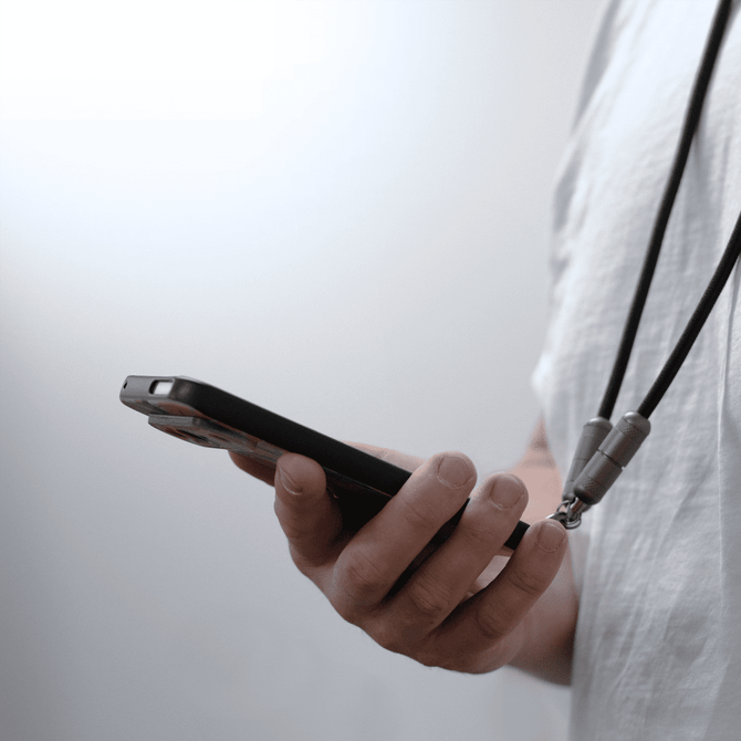 A black lanyard with charging connectors attached, holding a smartphone in a person's hand.