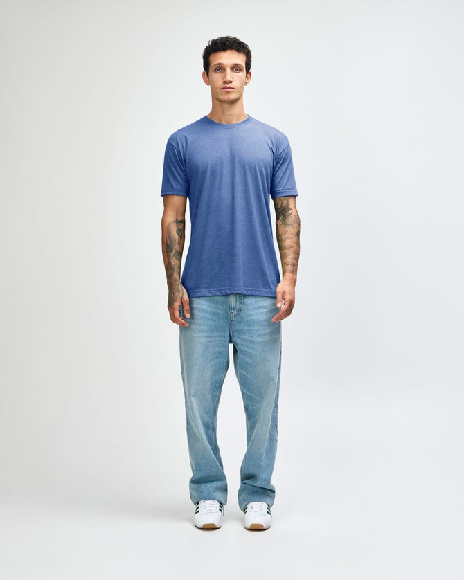 A man wearing a blue American Apparel tri-blend T-shirt and light blue jeans, standing against a plain background.