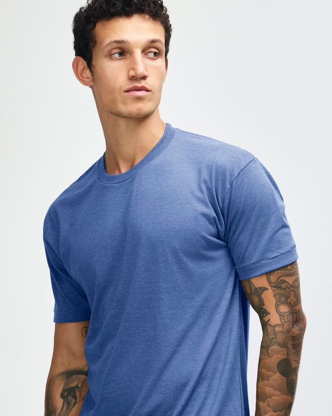 A blue tri-blend t-shirt on a model with tattoos, featuring a simple design and a logo.