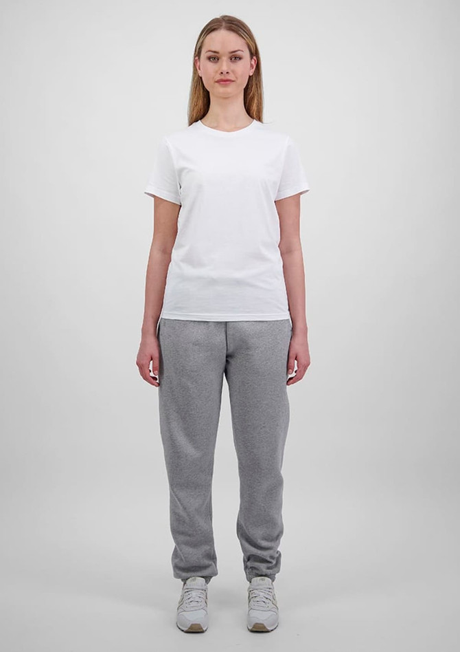 A woman wears a plain white t-shirt and grey track pants, standing against a light grey background. The pants have a logo.