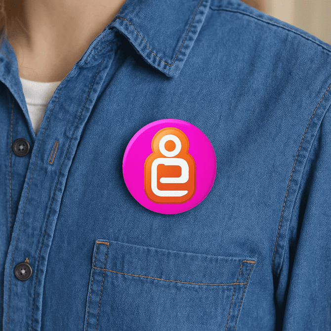 A 32mm button badge in pink with a circular design, displayed on a denim shirt pocket.