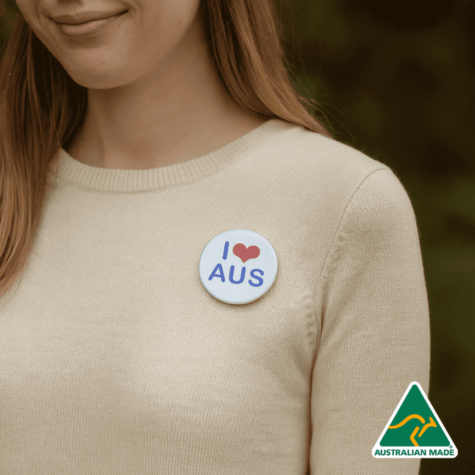 A 56mm button badge featuring a white background with blue text and a heart design, worn on a person's clothing.