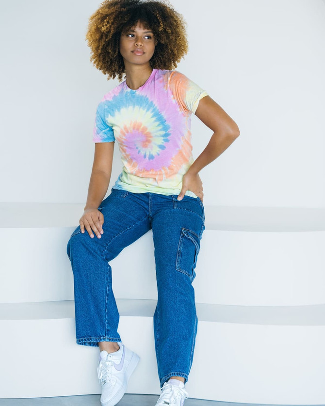 A tie-dye adult T-shirt in pastel colours, featuring a spiral pattern, worn with casual blue jeans and white sneakers.