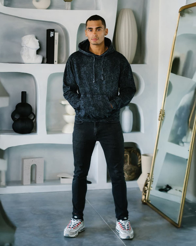 A model wears a dark mineral wash pullover hoodie paired with black jeans and stylish sneakers, set against a modern background.