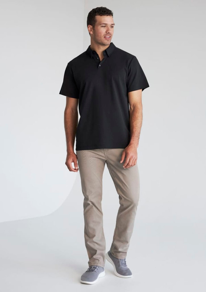 A man wearing a black short sleeve polo shirt and light grey trousers, featuring a logo on the polo.