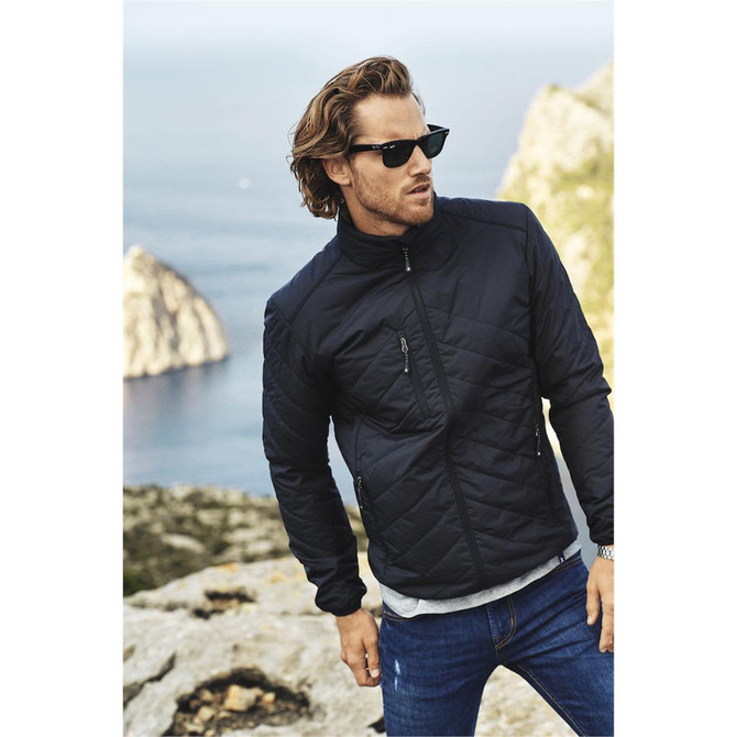 A quilted black jacket with a zip, worn by a man with sunglasses, set against a scenic rocky background.