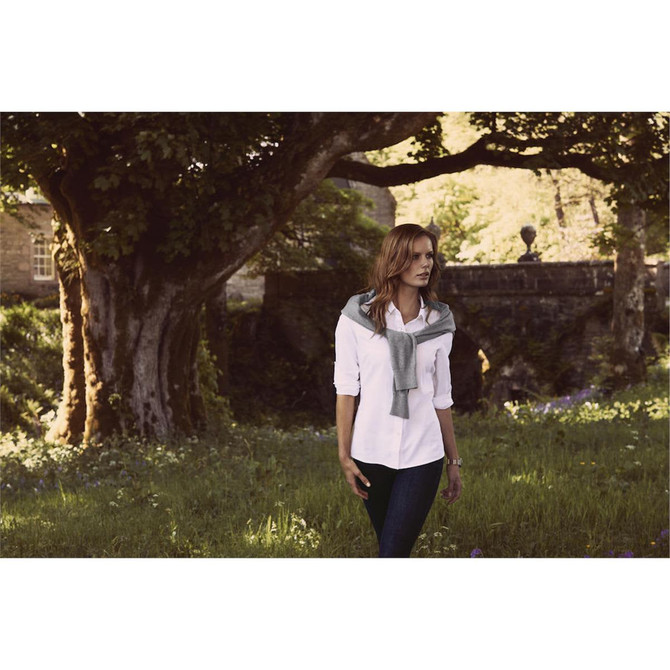 White button-up blouse worn by a woman with a grey sweater draped over her shoulders, standing in a grassy area with trees.