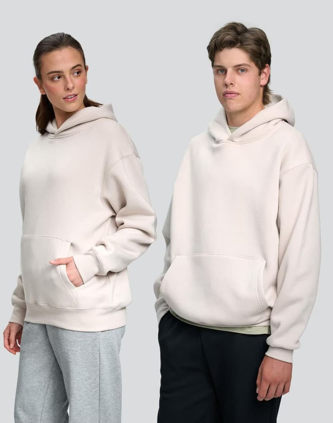 Unisex premium fleece oversized hoodie in light beige, featuring a front pocket and a hood. Logos included.