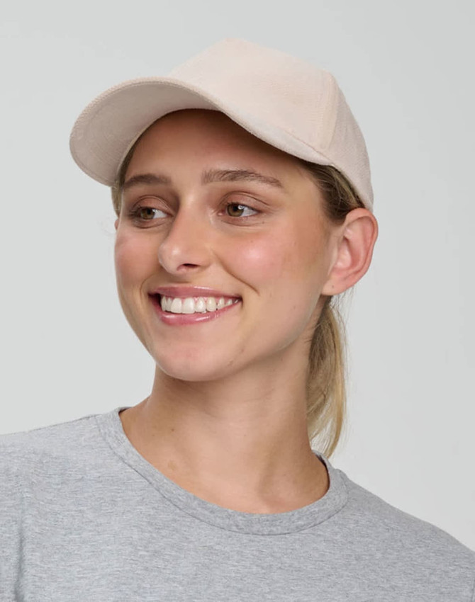 A beige Jacquard Texture 5 Panel Cap worn by a smiling individual, featuring a logo on the front.