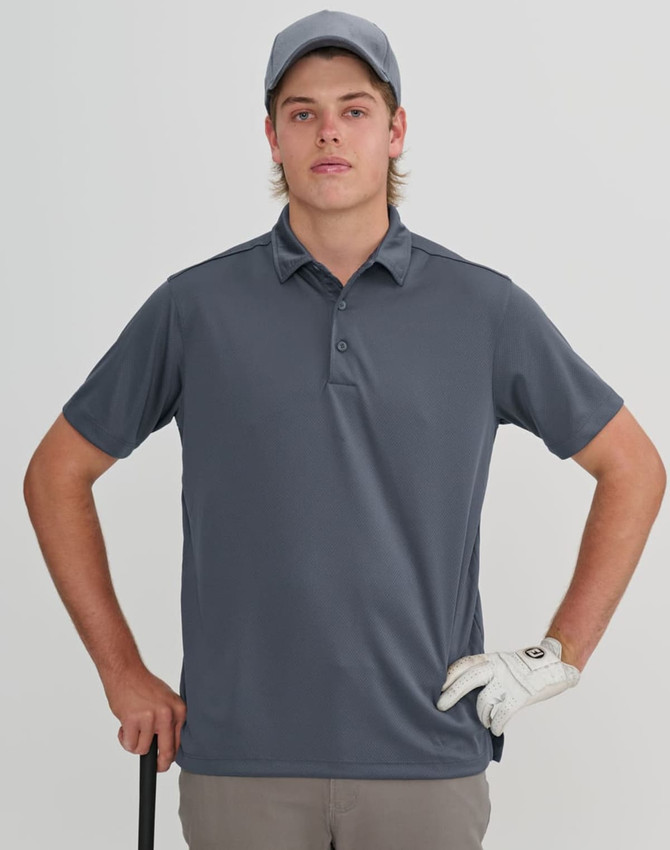 A young man in a grey polo shirt and cap holds a golf club, wearing a golf glove. The background is neutral.