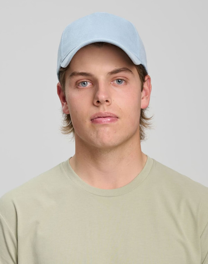 A light blue jacquard texture 5 panel cap worn by a young man, paired with a beige T-shirt.