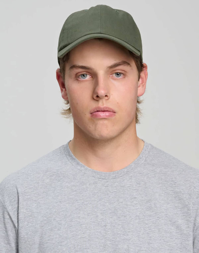 A green cotton twill unstructured cap worn by a young man in a grey t-shirt, featuring a logo.