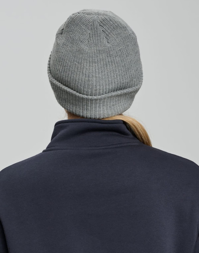 A grey cable knit beanie with a rolled cuff, seen from the back, worn by a person in a navy top.