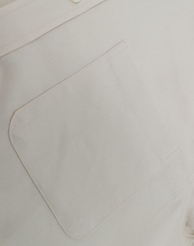 A close-up of a light-coloured cotton blend shirt featuring a back pocket and a button detail.