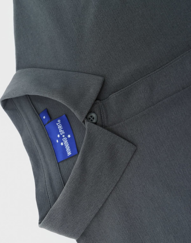 A grey polo shirt featuring a collar and a button, with a tag showing branding.
