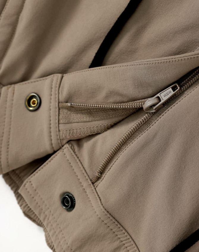 A close-up of beige work pants featuring zippers and button details, designed for flexibility and durability.