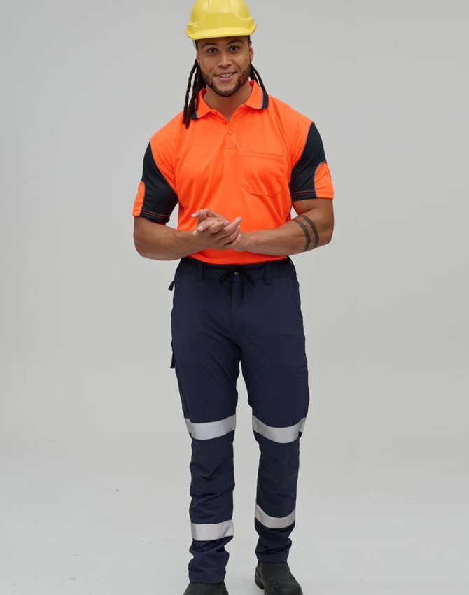 A man wearing a high-visibility orange polo shirt and navy work pants with reflective tape, along with a yellow hard hat.